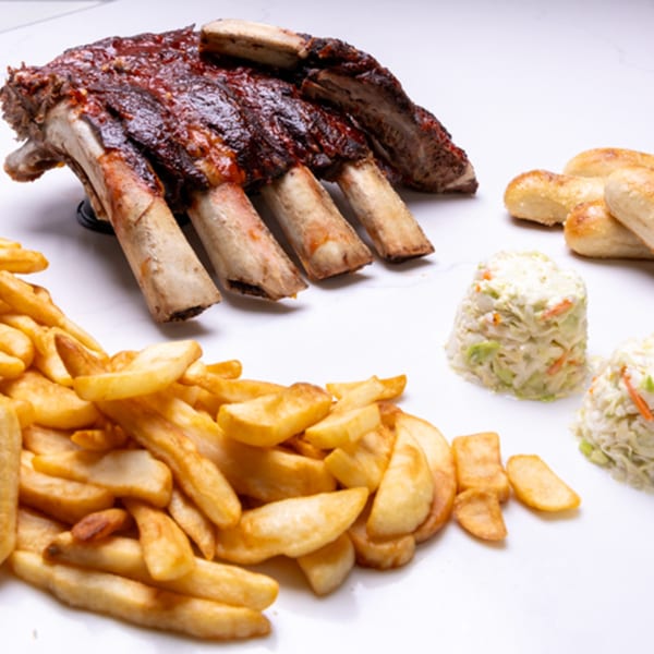 A rack of BBQ ribs, a pile of french fries, two servings of coleslaw, and breadsticks.