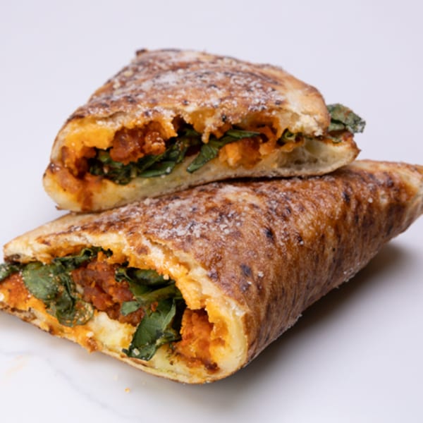 Two halves of a golden-brown calzone, filled with red sauce, cheese, and green spinach.