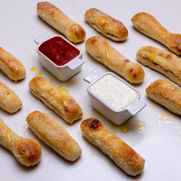 Pizza Place breadsticks with honey, parmesan, marinara, and ranch on a white surface.