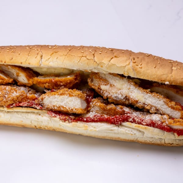 A close-up of a chicken parmesan hero sandwich with red sauce and grated cheese.