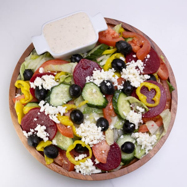 A vibrant salad with lettuce, tomatoes, cucumbers, olives, beets, feta, and dressing on a wooden plate.